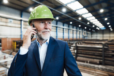 Geschäftsmann mit Schutzhelm, der in der Industrie mit einem Mobiltelefon spricht - JOSEF05724