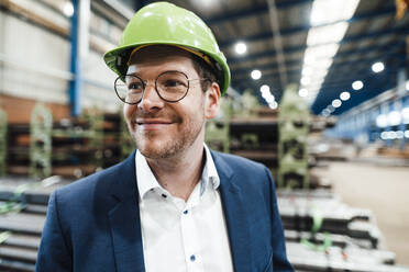 Lächelnder männlicher Fachmann mit Schutzhelm in einer Fabrik - JOSEF05727