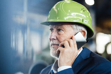 Male manager with hardhat talking on mobile phone in factory - JOSEF05758