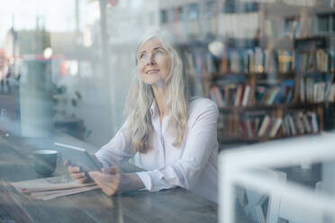 Nachdenkliche Geschäftsfrau mit digitalem Tablet, die durch das Fenster eines Cafés schaut - JOSEF05774