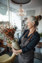 Lächelnde Café-Besitzerin betrachtet Blumenvase im Café - JOSEF05808