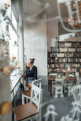 Frau schaut durch ein Fenster, während sie in einem Café sitzt - JOSEF05817