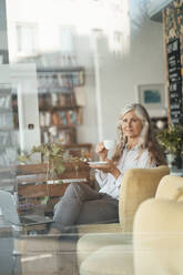 Geschäftsfrau hält Kaffeetasse und sitzt auf einem Stuhl in einem Café - JOSEF05837