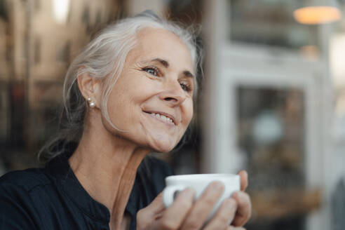 Smiling woman holding coffee cup in cafe - JOSEF05878