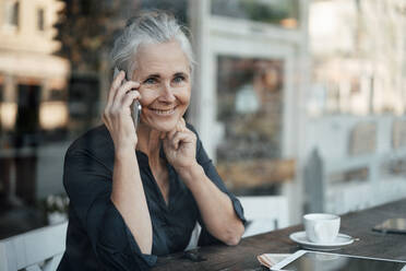 Lächelnde reife Geschäftsfrau, die in einem Café mit einem Mobiltelefon spricht - JOSEF05883