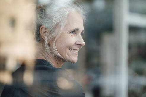 Lächelnde Frau mit grauem Haar in einem Café durch ein Glasfenster gesehen - JOSEF05897