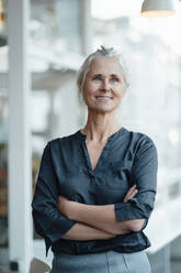 Confident female freelancer standing with arms crossed in coffee shop - JOSEF05905