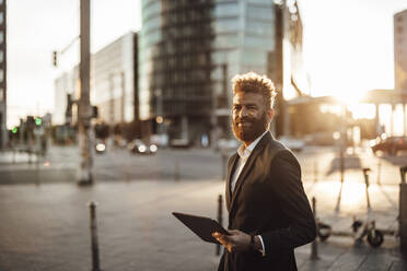 Lächelnder Geschäftsmann mit digitalem Tablet in der Stadt im Sommer - GUSF06362