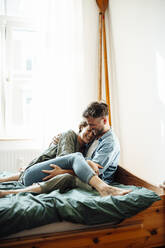 Cheerful couple embracing while sitting on bed at home - GUSF06400