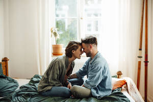 Couple touching foreheads while sitting on bed at home - GUSF06409
