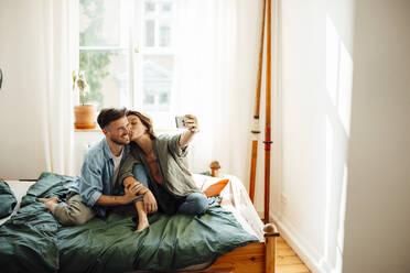 Frau küsst Mann und macht Selfie auf dem Bett zu Hause - GUSF06410