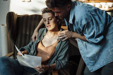 Male and female colleague looking at documents while working at home office - GUSF06421