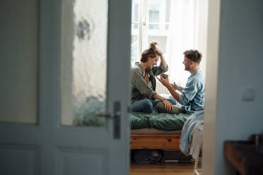 Woman with hand in hair sitting with man holding mug at home - GUSF06440