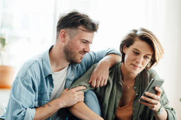 Man sitting near woman using smart phone at home - GUSF06449