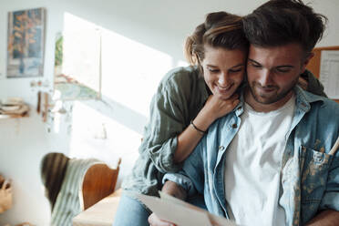 Woman embracing man while looking at document at home - GUSF06455