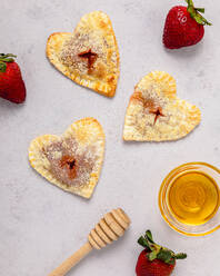 Studioaufnahme einer Schale mit Honig, Honiglöffel, Erdbeeren und frisch gebackenen herzförmigen Mini-Kuchen - FLMF00664