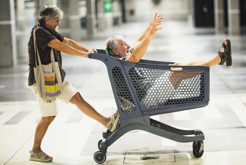 Ältere Frau, die einen Mann mit einem Einkaufswagen in einer Tiefgarage schiebt - SIPF02353