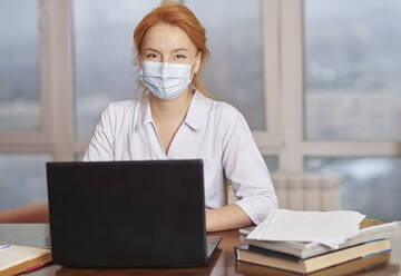 Mitarbeiterin des Gesundheitswesens mit Gesichtsschutzmaske sitzt mit Laptop im Krankenhaus - AZF00349