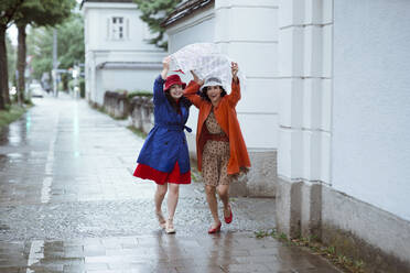 Surprised female tourists holding city map over head while running during rain - AANF00001