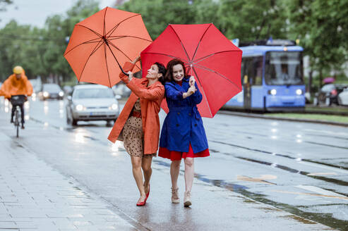 Frau, die mit einem Regenschirm kämpft, während sie mit einer Freundin bei Regen auf der Straße geht - AANF00005