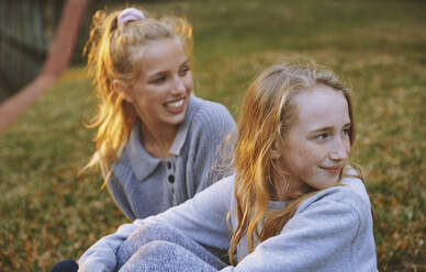 Girls looking away while sitting on grass in park - AZF00364