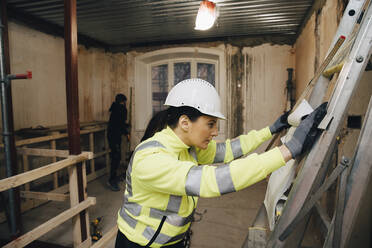 Female building contractor reading blueprint while working at site - MASF25134