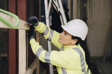 Female engineer marking on wooden plank while working at site - MASF25140