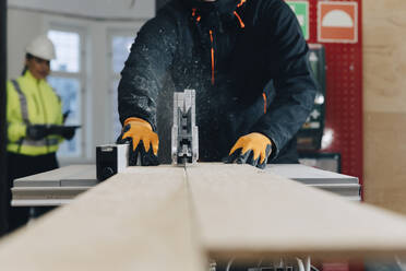 Mittelteil eines männlichen Arbeiters, der auf einer Baustelle eine Tischsäge zum Schneiden von Holzbrettern benutzt - MASF25150
