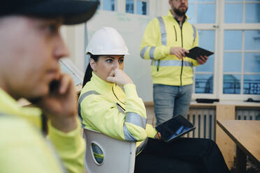 Nachdenkliche Bauunternehmerin, die während einer Besprechung mit einem digitalen Tablet im Büro sitzt - MASF25162
