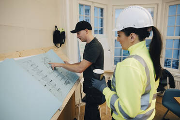 Männlicher Bauarbeiter bespricht einen Grundriss mit einer Bauunternehmerin im Büro - MASF25166
