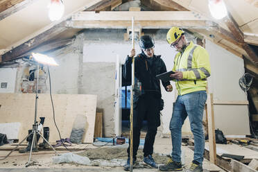 Männliche Bauarbeiter diskutieren über ein digitales Tablet während der Arbeit auf der Baustelle - MASF25178