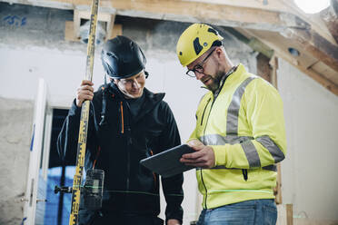 Male construction workers discussing over digital tablet while working at site - MASF25180