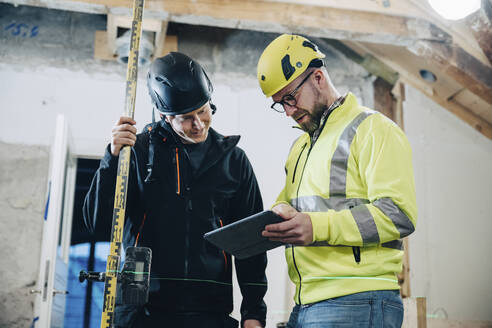 Männliche Bauarbeiter diskutieren über ein digitales Tablet während der Arbeit auf der Baustelle - MASF25180