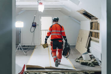 Rear view of male worker carrying construction equipment while working at site - MASF25181