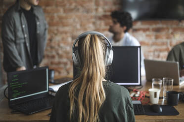 Weiblicher Hacker mit Kopfhörern bei der Arbeit am Computer im Büro - MASF25186
