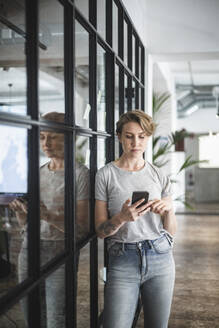 Unternehmerin mit Smartphone an der Wand im Kreativbüro - MASF25190