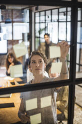 Businesswoman sticking adhesive notes during meeting in board room - MASF25200