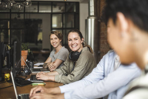 Happy male and female colleagues talking while working at startup company - MASF25205