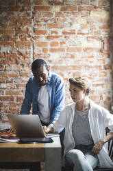 Male and female colleagues using laptop in office - MASF25230