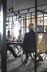 Female entrepreneur discussing with colleagues seen through doorway of startup company - MASF25292