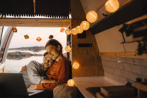 Homosexuelles Paar, das in einem beleuchteten Wohnmobil einen Film auf einem Laptop ansieht - MASF25310