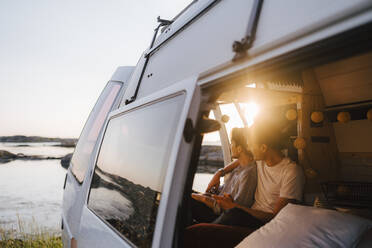 Gay couple spending leisure time in camping van at lakeshore - MASF25353