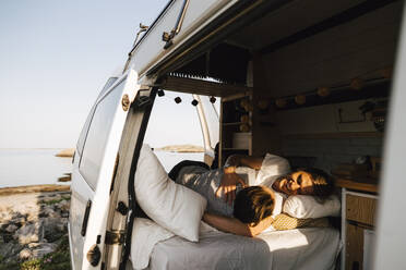 Gay couple resting in camping van at lakeshore during vacation - MASF25371