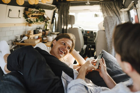 Mid adult man sharing smart phone with boyfriend in camping van - MASF25375