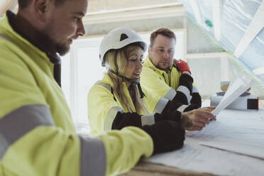 Female building contractor discussing over floor plan with male colleagues at construction site - MASF25428
