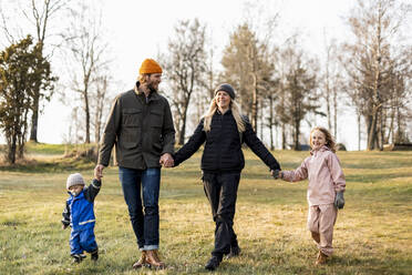 Fröhliche Familie in voller Länge, die sich beim gemeinsamen Spaziergang im Park an den Händen hält - MASF25524