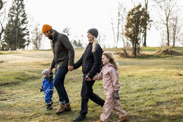 Glückliche Familie in voller Länge, die sich beim gemeinsamen Spaziergang im Park an den Händen hält - MASF25525