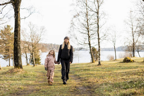 Frau in voller Länge mit Tochter spazieren gehend und Hände haltend im Park - MASF25527