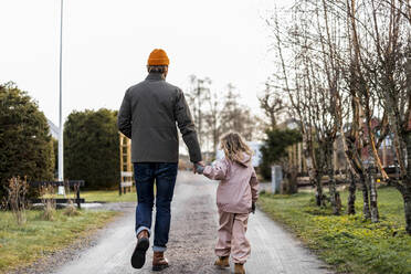 Gesamtansicht von hinten Vater und Tochter, die sich beim Gehen auf der Straße an den Händen halten - MASF25534