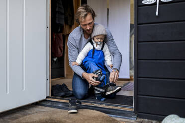 Mittlerer Erwachsener, der seinem Sohn beim Anziehen der Schuhe an der Tür hilft - MASF25547